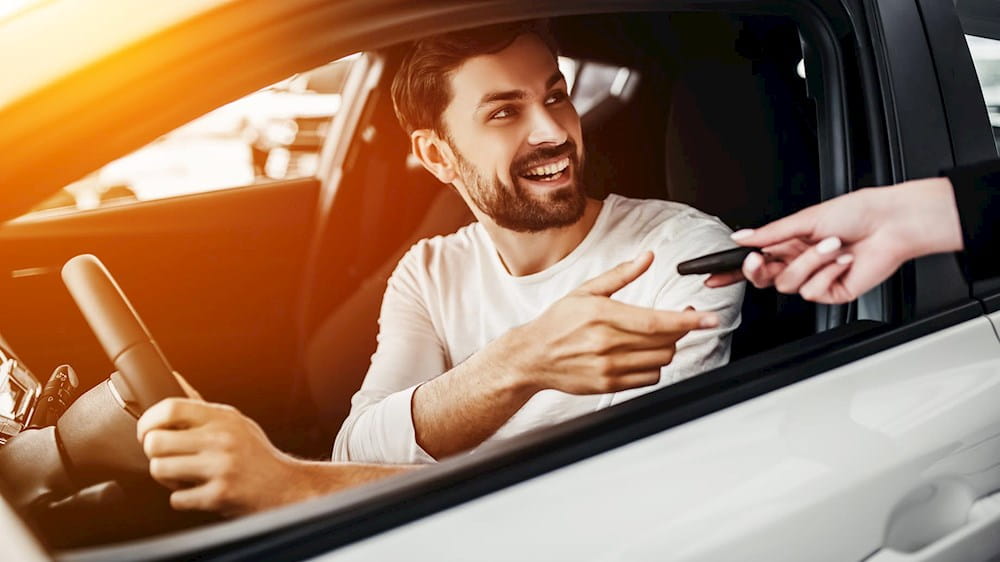 A man in a car smiling as he is handed a key